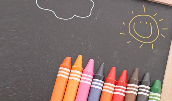Colorful crayons beside a chalk drawing of a smiling sun
